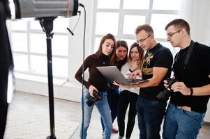 photographe expliquant la prise de vue à son équipe dans le studio et regardant sur un ordinateur portable. parler à ses assistants tenant un appareil photo lors d'une séance photo. travail d'équipe et remue-méninges.