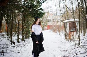 modèle brune à longues jambes à la mode dans une longue cape noire et un chapeau en plein air le jour de l'hiver. photo