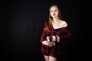 jeune femme au foyer en robe à carreaux avec casserole et cuillère de cuisine isolée sur fond noir. photo