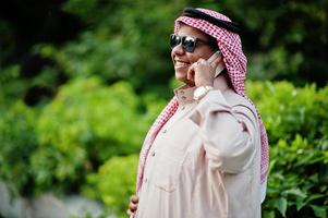 homme d'affaires arabe du moyen-orient posé dans la rue avec des lunettes de soleil, parlant au téléphone mobile. photo