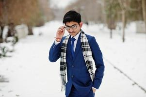 homme étudiant indien élégant en costume, lunettes et écharpe posé à la journée d'hiver en plein air. photo