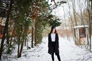 modèle brune à longues jambes à la mode dans une longue cape noire et un chapeau en plein air le jour de l'hiver. photo