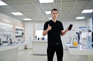 vendeur homme consultant professionnel en téléphonie mobile dans un magasin de technologie ou un magasin tenir un nouveau smartphone à portée de main et montrer le pouce vers le haut. photo