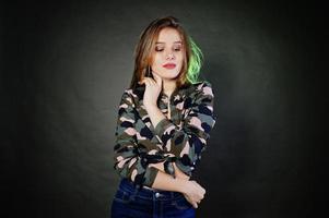 belle fille brune porte une chemise militaire et un jean, posant au studio sur fond gris. portrait de modèle de studio. photo