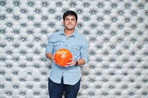 homme asiatique élégant en chemise jeans debout avec boule de bowling à portée de main sur fond de mur argenté. photo