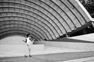 incroyable femme modèle afro-américaine en pantalon vert et chapeau noir posé en plein air contre le hall de l'arène. photo