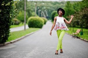 incroyable femme modèle afro-américaine en pantalon vert et chapeau noir posé avec différentes émotions au parc. photo