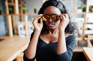 gros plan le visage d'une fille afro-américaine en lunettes de soleil posées au café moderne. photo