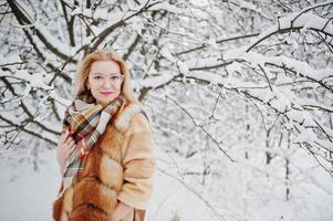 portrait d'une fille blonde à lunettes, manteau de fourrure rouge et écharpe le jour de l'hiver. photo