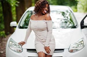 femme afro-américaine posée contre une voiture blanche sur une route forestière. photo