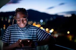jeune homme afro dans la rue la nuit en utilisant le téléphone photo