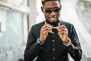 chic bel homme afro-américain en chemise noire avec chaîne en or et lunettes de soleil. photo