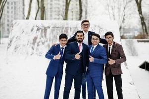 groupe de cinq hommes d'affaires indiens en costumes posés en plein air en journée d'hiver en europe, montrer le pouce vers le haut. photo