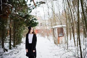 modèle brune à longues jambes à la mode dans une longue cape noire et un chapeau en plein air le jour de l'hiver. photo