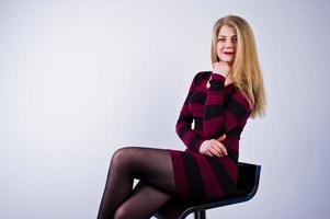 portrait d'une jeune femme en robe violette rayée assise sur la chaise dans le studio. photo