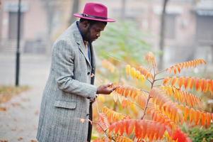 élégant modèle d'homme afro-américain en manteau gris, cravate de veste et chapeau rouge contre les feuilles jaunes humeur d'automne. photo