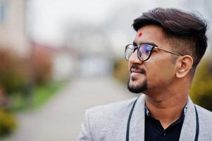 gros plan tête d'homme indien élégant avec bindi sur le front et lunettes, porter sur costume posé à l'extérieur. photo