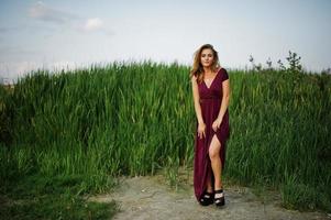 femme sensuelle blonde en robe marsala rouge posant dans les roseaux. photo