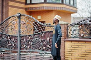 homme africain riche en vêtements traditionnels élégants et chapeau posé sur fond extérieur son manoir. photo