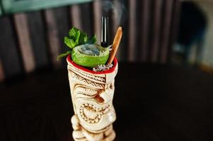 cocktail alcoolisé à la menthe et au citron vert avec feu dans un verre de terre vaudou à l'origine sur une table de bar. photo