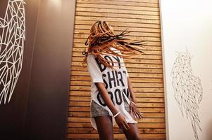 belle femme africaine dans des vêtements décontractés élégants posant contre le mur des ailes d'ange. elle bouge ses cheveux dreadlocks. photo