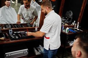 jeune homme barbu se coupe les cheveux par un coiffeur assis sur une chaise au salon de coiffure. âme de barbier. photo