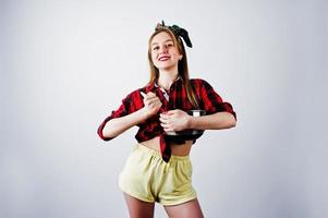 jeune femme au foyer drôle en chemise à carreaux et short jaune pin up style avec casserole et cuillère de cuisine isolé sur fond blanc. photo