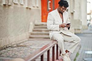 homme afro élégant en costume beige old school avec téléphone portable à portée de main. jeune homme africain à la mode en veste décontractée sur torse nu. photo