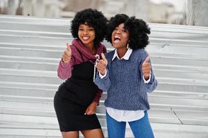 deux femmes afro-américaines aux cheveux bouclés portent des chandails posés le jour de l'hiver, montrent les pouces vers le haut. photo