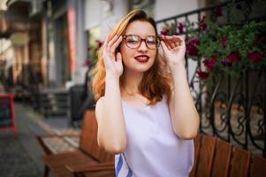 jolie femme rousse à lunettes posant dans la rue de la ville de printemps. photo