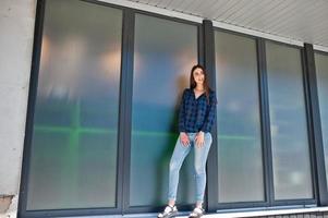 portrait de jeune fille brune en chemise à carreaux bleu contre de grandes fenêtres. photo