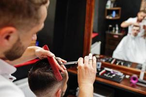 jeune homme barbu se coupe les cheveux par un coiffeur assis sur une chaise au salon de coiffure. âme de barbier. photo