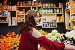 fille en rouge tenant différents légumes sur le magasin de fruits. photo