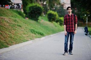 jeune étudiant indien en chemise à carreaux rouge et jeans avec sac à dos posé dans la rue. photo