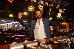 bel homme arabe bien habillé avec un verre de whisky et de cigare posé au pub. photo