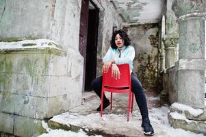 élégant modèle de taille plus afro-américain assis sur une chaise rouge en plein air. photo