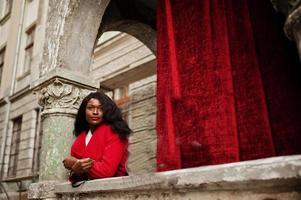 élégante femme afro-américaine en manteau rouge posée contre de vieilles colonnes. photo