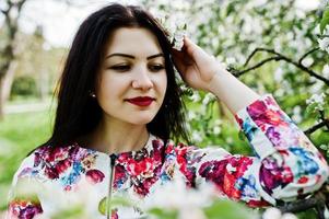 portrait de printemps d'une jeune fille brune au jardin de fleurs vertes. photo