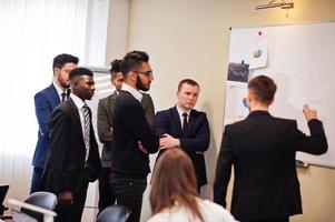 une équipe commerciale multiraciale s'adressant à une réunion autour d'une table de conférence et rédige un plan à bord. photo