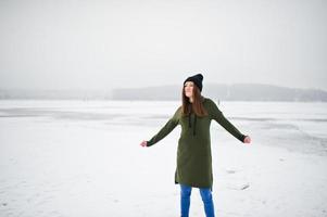 fille drôle portant un long sweat-shirt vert, un jean et un couvre-chef noir, au lac gelé en hiver. photo