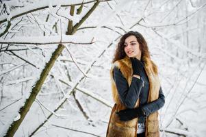 élégance bouclée fille en manteau de fourrure au parc forestier enneigé en hiver. photo