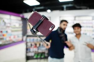 photo en gros plan d'un téléphone mobile sur un bâton monopode contre deux indiens mans client acheteur aking selfie. concept de peuples et de technologies d'asie du sud. magasin de téléphonie mobile.