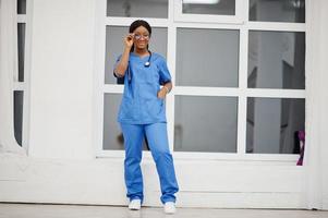 portrait d'une jeune femme médecin afro-américaine heureuse pédiatre en uniforme bleu et stéthoscope contre la fenêtre de l'hôpital. soins de santé, médecine, spécialiste de la médecine - concept. photo