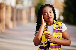 élégantes femmes afro-américaines en veste jaune posées dans la rue avec une boisson chaude dans une tasse en papier jetable. photo