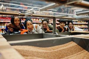 groupe de cinq femmes africaines amusantes avec des caddies choisissent des gruaux de sarrasin au supermarché. photo