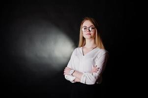 portrait en studio d'une femme d'affaires blonde à lunettes, chemisier blanc et jupe noire sur fond sombre. femme réussie et concept de fille élégante. photo