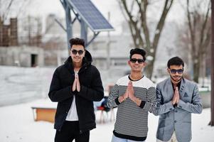 groupe de trois jeunes hommes indiens occasionnels portant des lunettes de soleil posées le jour de l'hiver, montre namaste. photo