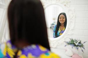 modèle de femme afro-américaine élégance porter des vêtements colorés. femmes afro chics dans la chambre regardant le miroir. photo