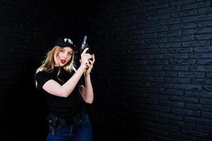 agent féminin du fbi en casquette et avec arme à feu au studio contre un mur de briques sombres. photo