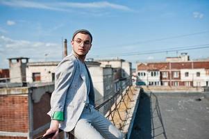 homme macho élégant rêveur en costume gris, chapeau et lunettes posés sur le toit. photo